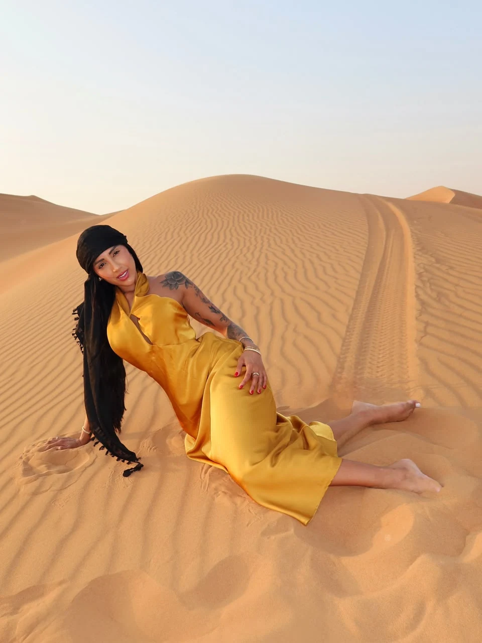 Woman in a yellow dress seated on golden desert dunes
