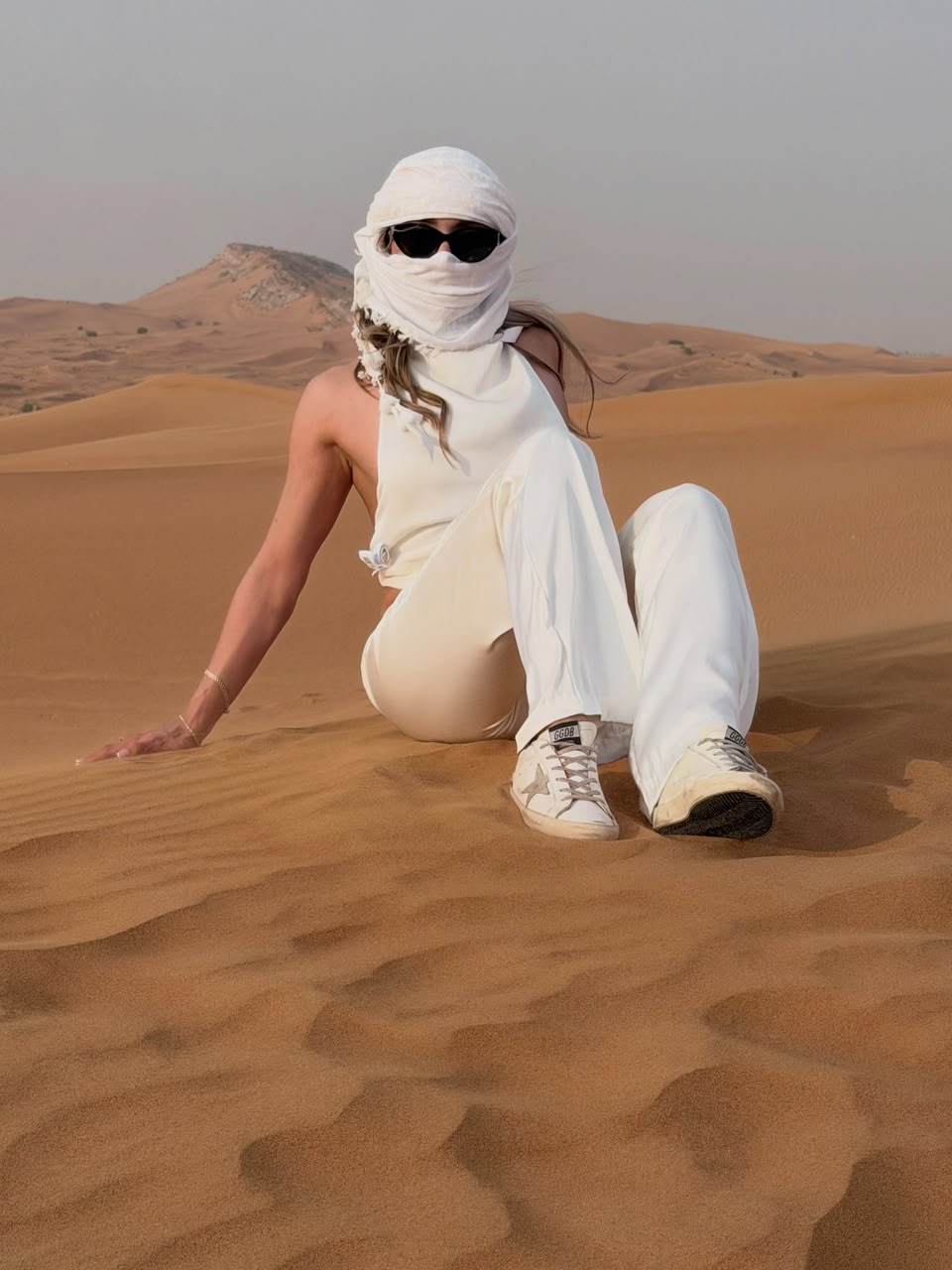 Visitor in white outfit sitting on sandy dunes in Dubai